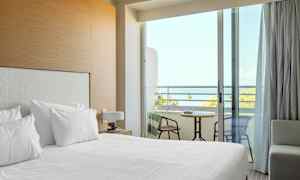 Ett hotellrum med bäddad säng och en balkong med utsikt över havet. (AI-genererad text)