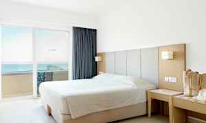 Ett hotellrum med en dubbelsäng nära fönster med utsikt över havet. (AI-genererad text)