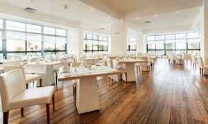 En modern och ljus restaurang med stora fönster och dukade bord. (AI-genererad text)