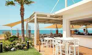 En utomhusrestaurang med bord och stolar, utsikt över havet och klarblå himmel. (AI-genererad text)