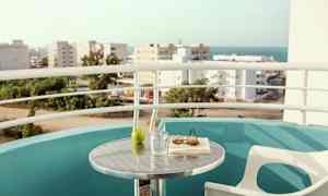 En balkong med utsikt över stad och hav. Ett bord med ett glas, en grön äpple, en bok och solglasögon. (AI-genererad text)