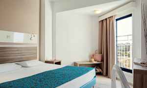 Hotellrum med en bäddad säng, nattduksbord och en balkongdörr. (AI-genererad text)