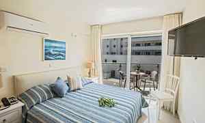 Ett hotellrum med en dubbelsäng, dekorerad i blå nyanser, och en balkong med möbler som vetter mot en angränsande byggnad. (AI-genererad text)