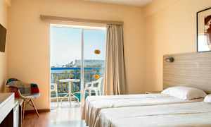 Ett hotellrum med två enkelsängar, en stol, TV, samt en balkong med utsikt. (AI-genererad text)