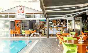 Utomhusområden med bord och stolar vid en pool, med en bar och matställe i bakgrunden. (AI-genererad text)