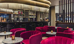 En elegant hotellbar med röda stolar och marmorbord framför en välutrustad bardisk. (AI-genererad text)