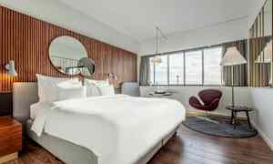 Ett modernt hotellrum med en stor säng, en rund spegel på väggen och fönster med utsikt. (AI-genererad text)