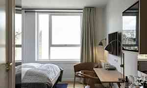 Bilden visar ett modernt hotellrum med en säng, ett skrivbord, en stol och ett stort fönster. (AI-genererad text)