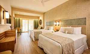 Hotellrum med två sängar, sittgrupp och ljusa möbler. (AI-genererad text)