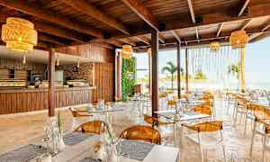 En modern restaurang med trämöbler, gula lampor och utsikt över havet. (AI-genererad text)