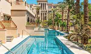 En lång smal pool omgiven av palmer och byggnader med arabisk arkitektur. (AI-genererad text)