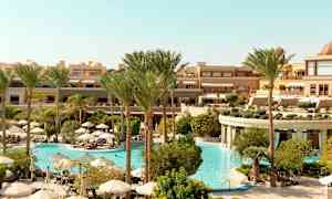 Ett hotellområde med en stor pool omgiven av palmer och parasoller. (AI-genererad text)