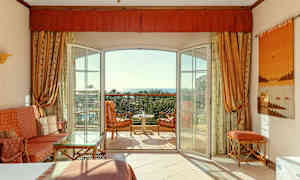 Ett hotellrum med öppen balkongdörr, sittmöbler och utsikt mot havet. (AI-genererad text)