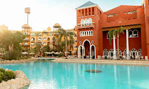 Hotellbyggnad med röd fasad vid ett poolområde med solstolar och parasoller. (AI-genererad text)