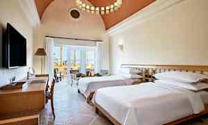 Hotellrum med två enkelsängar, skrivbord och sittgrupp vid balkongen. (AI-genererad text)