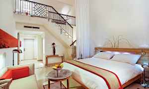 Modernt inredd hotellsvit med dubbelsäng, sittgrupp och trappa till loft. (AI-genererad text)