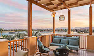 Terrass med soffgrupp och utsikt över en kanal och byggnader i solnedgång. (AI-genererad text)