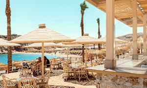 Uteservering med bambustolar och parasoll nära stranden med blått vatten. (AI-genererad text)