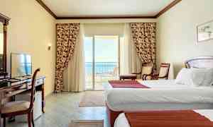 Hotelrum med vita väggar, två enkelsängar och en balkong med utsikt mot havet. (AI-genererad text)