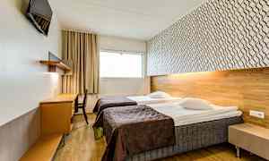 Ett hotellrum med två enkelsängar, ett skrivbord och en väggmonterad TV. (AI-genererad text)