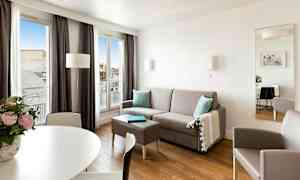 Ett modernt, ljust vardagsrum med grå soffa, bord, fåtölj och stora fönster som släpper in naturligt ljus. (AI-genererad text)