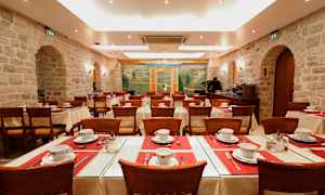 En matsal med dukade bord och stolar, omgiven av stenväggar och dekorerad med en muralmålning. (AI-genererad text)