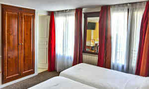 Ett hotellrum med två sängar, vita lakan och en trägarderob bredvid ett fönster med röda gardiner. (AI-genererad text)