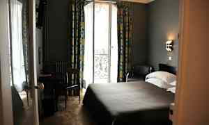 Ett hotellrum med en dubbelsäng, ett bord och en stol, samt en glasdörr med utsikt och gardiner. (AI-genererad text)