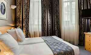 Ett hotellrum med två enkelsängar, ljusa gardiner och en dekorativ sänglöpare. (AI-genererad text)