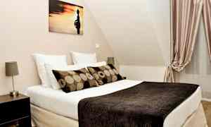 Ett sovrum med en säng, kuddar, konst på väggen och gardiner. (AI-genererad text)