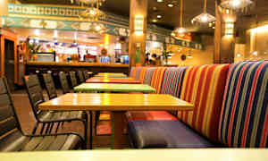 En restaurang med färgglada bord och stolar, samt randiga bänkseter. (AI-genererad text)