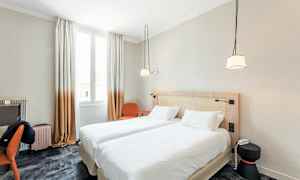 Ett hotellrum med två enförbundna enkelsängar, ett skrivbord, en stol och fönster med ljusinsläpp. (AI-genererad text)