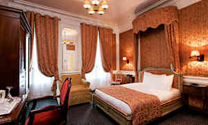 Ett hotellrum med en inredning i klassisk stil, med en dubbelsäng, röda gardiner och en fåtölj. (AI-genererad text)