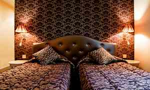 Två bäddar med dekorativa överkast och kuddar framför en mörk mönstrad vägg. (AI-genererad text)