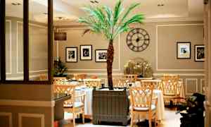 Inne i ett elegant café med ett centralt placerat palmerträd och dekorativa inslag. (AI-genererad text)