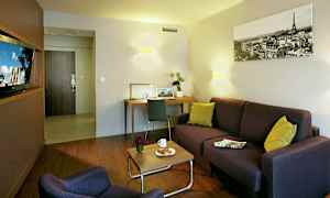 Ett vardagsrum med en soffa, fåtölj, soffbord med kaffekopp och croissant, skrivbord och dekorativa detaljer. (AI-genererad text)