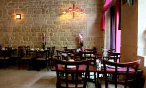 Ett restaurangutrymme med bord och stolar, samt dekorationsväxter framför en stenmur. (AI-genererad text)