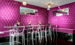 En modern och färgstark restaurang eller lounge med fuchsiafärgad vadderad väggpanel, genomskinliga stolar och spegeldekorationer. (AI-genererad text)