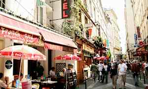 En livlig gata i en stad med uteserveringar och skyltar från olika restauranger och hotell. (AI-genererad text)