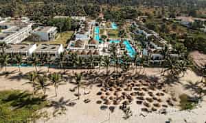 Flygfotografi av en resort med pooler, tropiska palmer och strand med parasoller. (AI-genererad text)