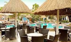 Stolar och bord vid en pool med halmtak. (AI-genererad text)