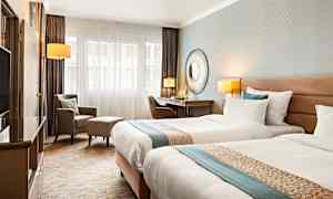 Ett hotellrum med två enkelsängar, skrivbord, stol och fåtölj. (AI-genererad text)