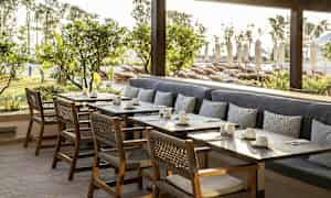 Uteplats med bord, stolar och sittbänk mot bakgrund av grönska och solstolar. (AI-genererad text)