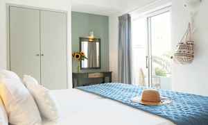 Ett ljust hotellrum med en bäddad säng, en solhatt på blått överkast och en dekorativt bord med spegel och en vas med solrosor. (AI-genererad text)