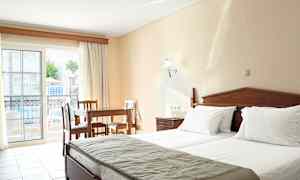 Ett hotellrum med två sängar, ett träbord och stolar, samt en balkong med utsikt över poolområdet. (AI-genererad text)