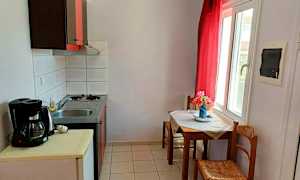 Ett litet kök med en diskbänk och spis samt ett bord med stolar intill ett fönster. (AI-genererad text)