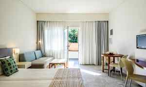 Hotellrum med bäddad säng, sittgrupp, rund matbord och balkongdörr. (AI-genererad text)