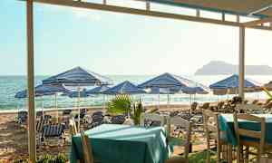 Strand med blå-vitrandiga parasoller och solstolar, bord i förgrunden. (AI-genererad text)