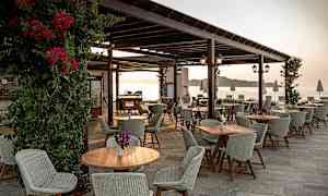 Uteservering med bord och stolar och utsikt mot havet. (AI-genererad text)