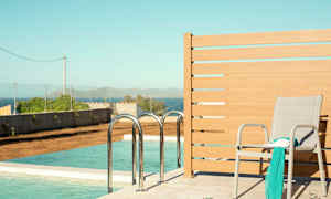 En solstol med en sjal och en bok står vid sidan av en pool med havsutsikt. (AI-genererad text)